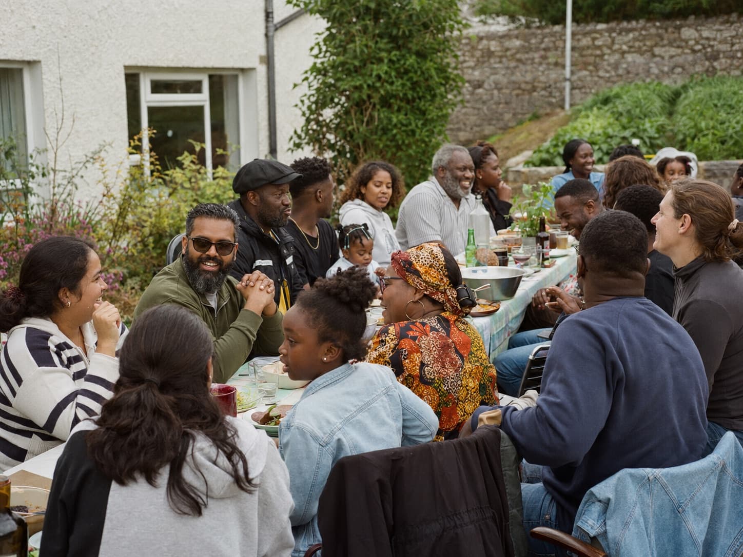 A multicultural group of neighbours of all ages sharing an outdoor meal together in Cornwall